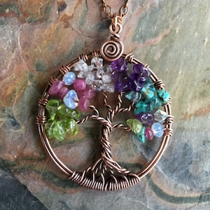 May include: A copper wire wrapped tree of life pendant necklace with a variety of colorful gemstones including amethyst, turquoise, peridot, and rose quartz.