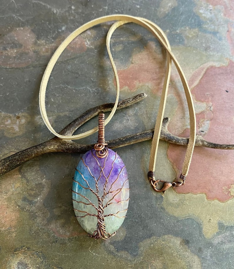 May include: A copper wire tree of life pendant with a colorful agate stone. The pendant is on a light brown leather cord.
