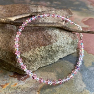 May include: A delicate pink and clear crystal necklace with a silver clasp. The necklace is made of small, faceted crystals that sparkle in the light.