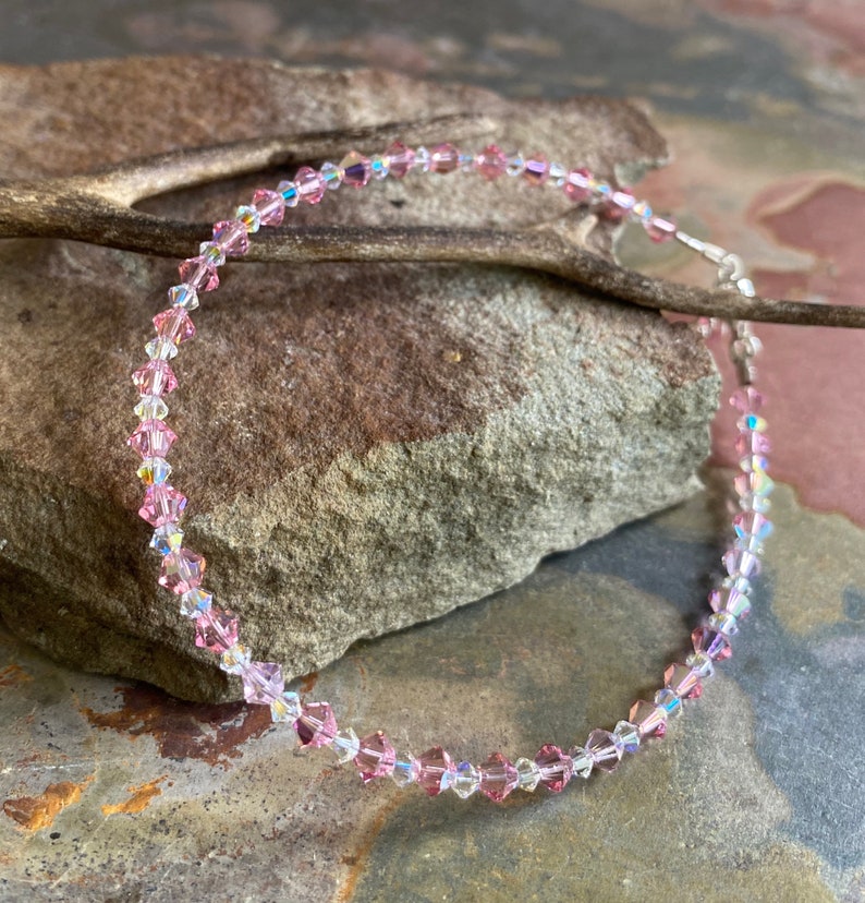 May include: A delicate pink and clear crystal necklace with a silver clasp. The necklace is made of small, faceted crystals that sparkle in the light.