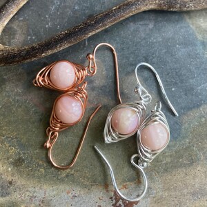 May include: A pair of earrings with pink opal stones wrapped in wire. One earring is made with copper wire and the other with silver wire.