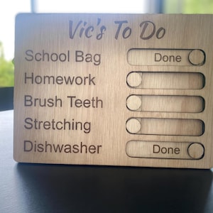 May include: Wooden "Vic's To Do" checklist with engraved text. The list includes "School Bag," "Homework," "Brush Teeth," "Stretching," and "Dishwasher." Each task has a slider to mark as "Done."