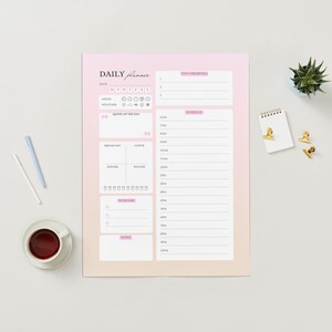 May include: A daily planner with a pink and peach gradient background, featuring sections for scheduling, notes, and a to-do list. The words "Daily Planner" are at the top. A cup of coffee, pens, and decorative items are arranged around the planner.