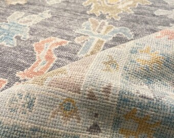 May include: Close-up of a gray rug with a detailed, colorful pattern. The design features floral and geometric shapes in shades of blue, pink, yellow, and beige. The rug has a soft, textured appearance, with a folded section revealing the underside.