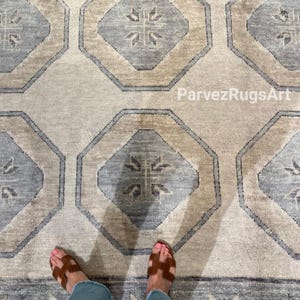 May include: A beige and blue patterned rug with geometric shapes. The rug features octagonal designs in beige and blue, with a central floral motif. The rug is made of a woven material and has a border. The text "ParvezRugsArt" is visible on the rug.