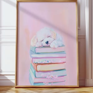 May include: A framed print featuring a sleeping white puppy atop a stack of colorful books. The artwork has a soft, pastel color palette with a pink background and a gold frame. The books are in shades of blue, pink, and yellow.