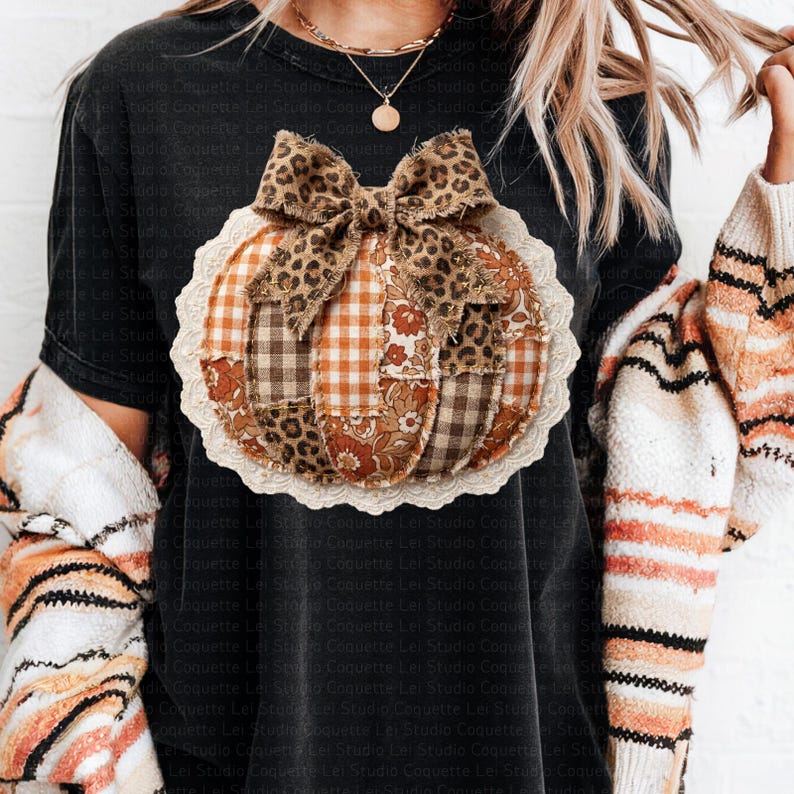 May include: Black t-shirt featuring a patchwork pumpkin design with a leopard print bow. The pumpkin is made of various fabrics in shades of brown, orange, and cream, with a white lace trim. A fall-themed graphic tee.