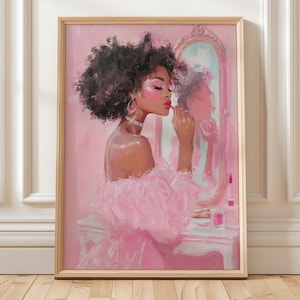 May include: A framed pink art print depicts a woman applying lipstick in front of a mirror. The woman is wearing a pink dress and jewelry. The artwork has a soft, painterly style with a focus on pink tones.