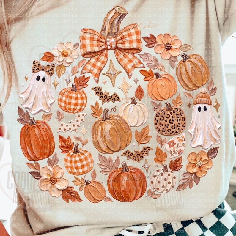 May include: A light-colored t-shirt featuring a circular graphic of pumpkins, ghosts, flowers, and bats. The design includes orange gingham and leopard print patterns on the pumpkins and bows, with small star accents scattered throughout the arrangement.