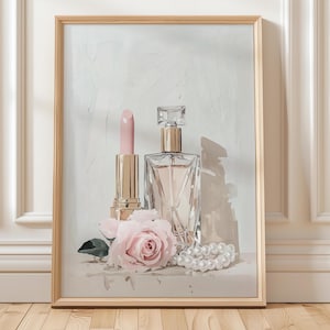 May include: A framed artwork featuring a lipstick, perfume bottle, pink rose, and a pearl necklace. The lipstick and perfume bottle have gold accents. The artwork is in a wooden frame and has a neutral background.