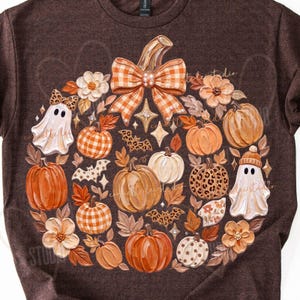 May include: A dark brown t-shirt featuring a large circular graphic of various pumpkins, two ghosts, flowers, and bats. The central pumpkin is topped with a large orange and white checkered bow. The design includes leopard print and plaid patterns.