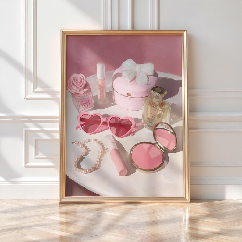 May include: A framed print featuring a collection of pink accessories. Items include heart-shaped sunglasses, a compact mirror, a pearl necklace, perfume bottles, a jewelry box with a bow, and a rose-shaped perfume bottle. The items are arranged on a white surface.