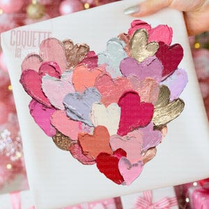 May include: A heart-shaped artwork composed of layered, textured brushstrokes in various shades of pink, red, gold, and white. The artwork is on a white surface, with the text "COQUETTE lei studio" visible. The overall theme is romantic and artistic.