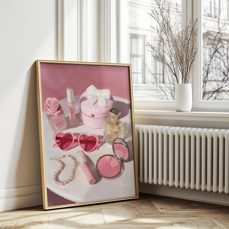 May include: A framed artwork featuring a still life of pink accessories. The composition includes heart-shaped sunglasses, a pearl necklace, a compact mirror, perfume bottles, and a gift box with a bow. A rose-shaped perfume bottle and lipstick are also visible.