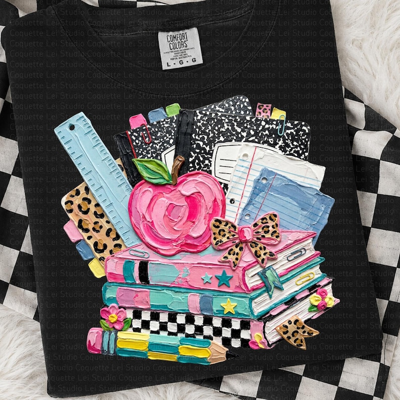 May include: Black crew neck sweatshirt with a colorful school-themed design. The design features a stack of books, an apple, a ruler, and notebooks. The design includes pink, blue, yellow, and leopard print accents. The sweatshirt has a Comfort Colors tag.