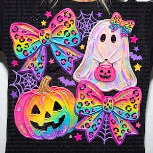 May include: A black t-shirt featuring a vibrant, textured graphic print of a rainbow-colored pumpkin, a ghost with a pink jack-o'-lantern bucket, and two large bows with a colorful leopard print pattern, accented by purple spiderwebs and stars.