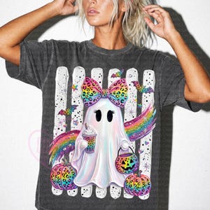 May include: A charcoal gray t-shirt featuring a graphic of a white ghost with a rainbow leopard print bow, holding a coffee cup and a jack-o'-lantern bucket. The design includes rainbow wings, two leopard print pumpkins, and bats.