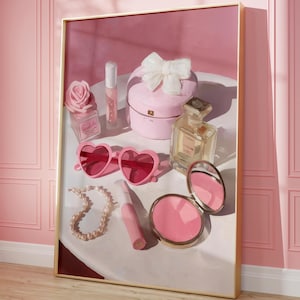 May include: A framed artwork featuring a collection of pink accessories. Heart-shaped sunglasses, a pearl necklace, a compact mirror, perfume, and a jewelry box with a bow are arranged on a white surface. A pink rose-shaped perfume bottle and lip gloss are also present.