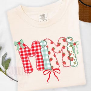 May include: Cream-colored t-shirt with the word "Mimi" in a patchwork design. The "M" is red and white gingham, the "i" is light green gingham, and the second "m" is pink with strawberry patterns. Each letter has a scalloped edge and a bow.