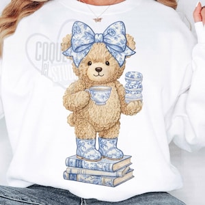 May include: A whimsical illustration of a teddy bear wearing a blue floral bow, boots, and holding a teacup and a stack of macarons. The bear stands on a stack of books with blue floral designs. The image has the text "COOL Let STUDIO".