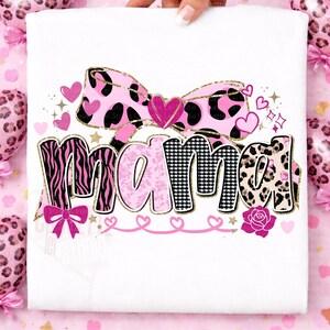 K&ouml;nnte beinhalten: Wei&szlig;es T-Shirt mit dem Wort "Mama" in einem rosa-schwarzen Design. Das Wort ist mit Zebra-, Blumen- und Leopardenmustern verziert. Das Design umfasst eine rosa Schleife, Herzen und eine goldene Glitzerumrandung.