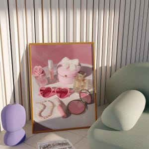 May include: A framed print featuring a collection of pink beauty products, including heart-shaped sunglasses, a compact mirror, and a perfume bottle. A pearl necklace and a small box with a bow are also visible. A lavender lamp is in the foreground.