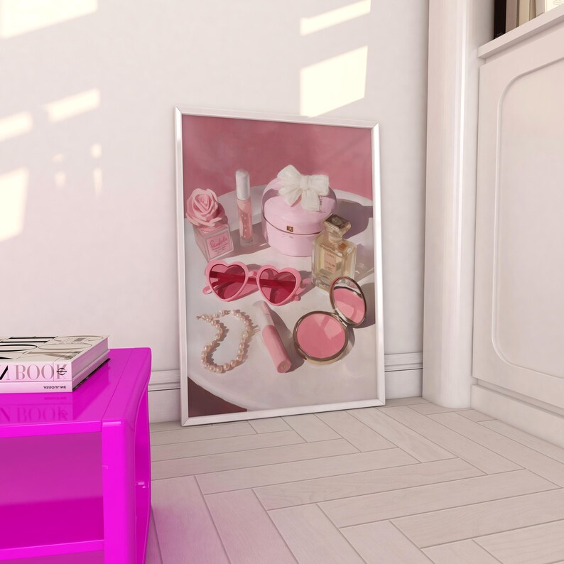 May include: A framed print featuring a collection of pink accessories. The items include heart-shaped sunglasses, a perfume bottle, a compact, a jewelry piece, a lipstick, and a small box with a bow. A pink rose and a small bottle are also visible.