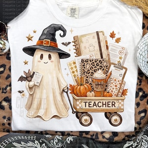 May include: A white t-shirt featuring a graphic of a ghost wearing a black witch hat and holding a paper, standing next to a wagon filled with school supplies, including a pumpkin, a coffee cup, notebooks, and papers with the text TEACHER.