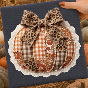 May include: A handmade fabric pumpkin decoration with a leopard print bow. The pumpkin is made of patchwork fabric in shades of orange, brown, and cream, with a white lace trim. A festive fall decoration.
