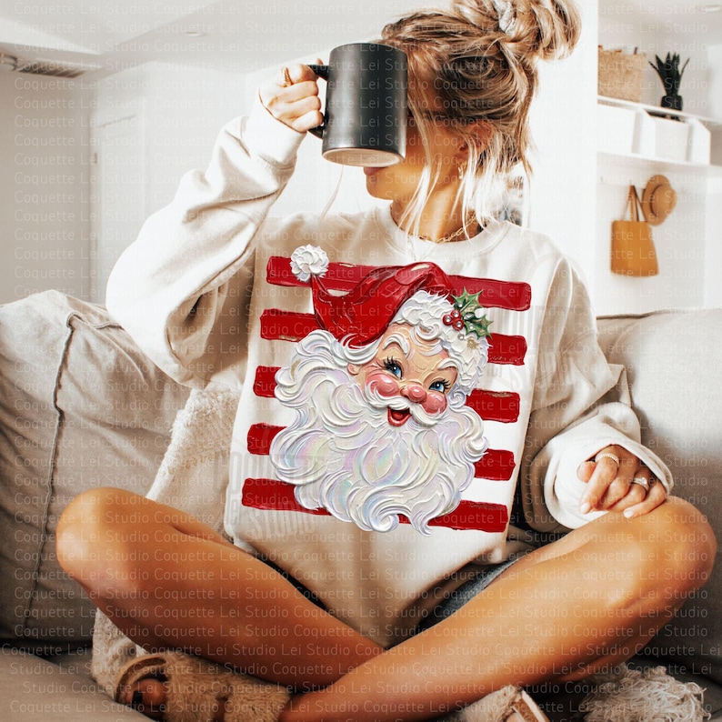 K&ouml;nnte beinhalten: Ein cremefarbenes Langarm-Sweatshirt mit einem Grafikdruck eines weihnachtlichen Santa-Claus-Gesichts im Vintage-Stil, mit roter M&uuml;tze und wei&szlig;em Bart, &uuml;berlagert von horizontalen roten Streifen. Das Sweatshirt hat einen Rundhalsausschnitt.