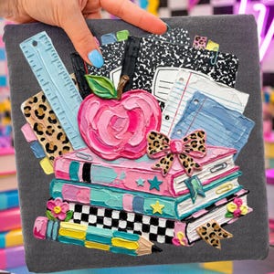 May include: A gray notebook cover adorned with a vibrant, textured design featuring a pink apple, stacked books, a ruler, and a leopard print bow. The design includes pencils, notebooks, and stars, evoking a school theme.