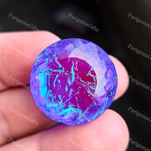 May include: A faceted, spherical gemstone with a vibrant color palette. The gem features a deep purple core with streaks of electric blue and turquoise, creating a mesmerizing play of light. The surface is cut to enhance its brilliance.