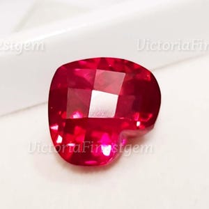 May include: A faceted, heart-shaped gemstone in a vibrant shade of red. The gem has a polished surface with multiple facets that catch the light, creating a sparkling effect. The gemstone is set against a white background.