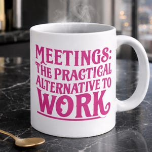 White ceramic mug with the phrase “Meetings: The Practical Alternative To Work” in bold pink text, styled on a black marble countertop in a luxury condo. Perfect gift for co-worker, colleague, boss - friend mum dad girlfriend boyfriend husband wife partner or special person in your life.