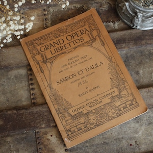 May include: A vintage opera libretto titled "Samson et Dalila" from 1936, featuring French and English text. The cover is a light brown color with ornate black lettering and illustrations. Published by Oliver Ditson Company, Boston.