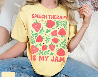 May include: Butter yellow t-shirt with the text "SPEECH THERAPY IS MY JAM" in pink and white. The shirt features a strawberry and leaf design in red, green, and yellow. The shirt is a casual, comfortable style.