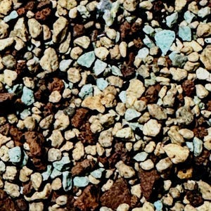 May include: Close-up of a mix of small, irregularly shaped rocks in shades of brown, tan, and light blue. The rocks have a rough texture and vary in size, creating a natural, earthy appearance. Ideal for gardening or landscaping.