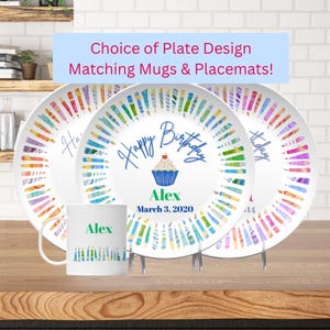 May include: White ceramic plates and a mug with a birthday theme. The plates and mug feature a colorful candle design and the text "Happy Birthday" with a cupcake illustration. The mug and one plate say "Alex" and "March 3, 2020".