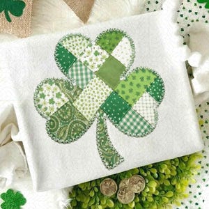 May include: A white rectangular pillow with a large shamrock design. The shamrock is made of various green patterned fabrics, including polka dots, floral prints, and gingham. The edges are stitched with a green zigzag stitch. Gold coins are at the bottom.