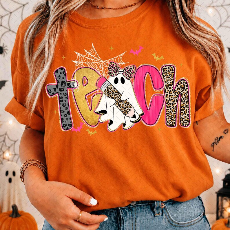 Peut inclure: Un t-shirt orange avec le mot TEACH &eacute;crit en grandes lettres color&eacute;es. Le T est en imprim&eacute; l&eacute;opard gris, le E est dor&eacute;, le A est un fant&ocirc;me blanc tenant un crayon l&eacute;opard, le C est rose et le H est en imprim&eacute; l&eacute;opard. Une toile d'araign&eacute;e est au-dessus.