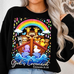 May include: Black sweatshirt featuring a colorful illustration of Noah's Ark with various animals, a rainbow, and the text "God's Covenant Genesis 9:16". The design includes giraffes, a zebra, a sloth, a tiger, and other animals.