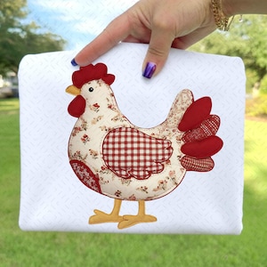 Könnte beinhalten: Ein weißes quadratisches Stoffstück mit einem dekorativen Hühner-Applikation. Das Huhn hat einen roten Kamm, Kehllappen und Schwanzfedern. Der Körper ist mit floralen und Vichy-Mustern versehen, mit gelben Füßen und einem gelben Schnabel.