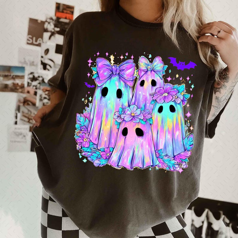 Op de afbeelding: Donkergrijs T-shirt met een kleurrijke illustratie van vier cartoongeesten. De geesten hebben strikken, bloemenkransen en zijn omringd door bloemen en vleermuizen. Het ontwerp maakt gebruik van een levendig kleurenpalet van paars, blauw en geel.