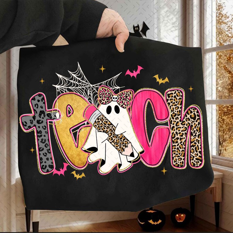 Peut inclure: Un sweat-shirt noir avec le mot TEACH &eacute;crit en lettres color&eacute;es et &agrave; motifs. La lettre A est remplac&eacute;e par un fant&ocirc;me blanc portant un n&oelig;ud &agrave; motif l&eacute;opard et tenant un crayon. Le motif inclut une toile d'araign&eacute;e, des chauves-souris et des &eacute;toiles.