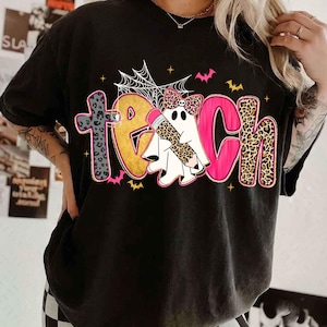Peut inclure: Un t-shirt noir avec le mot TEACH &eacute;crit en grandes lettres color&eacute;es. Le T est en imprim&eacute; l&eacute;opard gris, le E est dor&eacute;, le A est un fant&ocirc;me blanc avec un n&oelig;ud et un crayon l&eacute;opard, le C est rose et le H est en imprim&eacute; l&eacute;opard. Avec toiles d'araign&eacute;e et chauves-souris.
