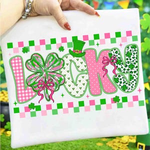 May include: White St. Patrick's Day themed design with the word "LUCKY" in pink, green, and white. The letter "L" is pink gingham, the "U" is a green shamrock, the "C" is white with green shamrocks, the "K" is pink, and the "Y" is green leopard print.