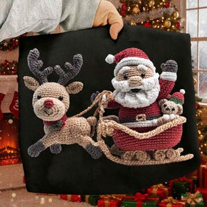 Peut inclure: Un sac fourre-tout noir sur le thème de Noël avec un Père Noël au crochet dans un traîneau tiré par un renne. Le Père Noël porte un costume et un chapeau rouges, et le renne a des bois et une écharpe rouge. Un petit ours en peluche est dans le traîneau.