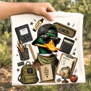 May include: A white t-shirt featuring a graphic of a mallard duck wearing a black baseball cap with the text "QUACK MODE" and sunglasses, holding a pencil in its beak. The design includes school supplies like a notebook, calculator, globe, backpack, and a clipboard with a "TO DO LIST" that reads "STUDY, READ, LEARN, REPEAT". A small notebook says "BIG IDEAS START HERE".
