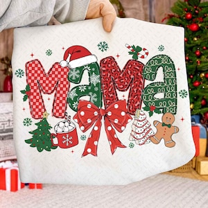 Könnte beinhalten: Ein weißes, weihnachtliches Dekokissen mit dem Wort "MAMA" in Rot, Grün und Leopardenmuster. Das Design umfasst einen Weihnachtsmannhut, Schneeflocken, eine Schleife, einen Weihnachtsbaum, eine Tasse heiße Schokolade und einen Lebkuchenmann.
