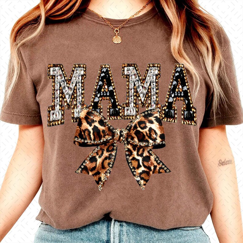 May include: A brown t-shirt with the word "MAMA" in a jeweled font and a leopard print bow. The shirt is short-sleeved and has a crew neck. The bow is embellished with rhinestones.